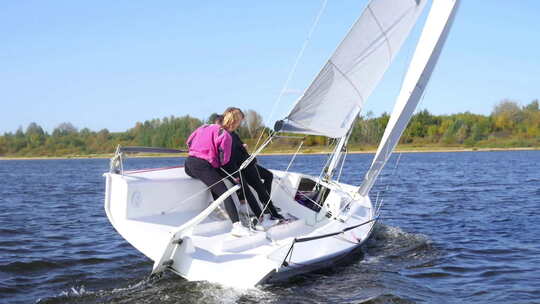 一个男人和两个女孩通过用脚控制帆来展示帆船的转弯