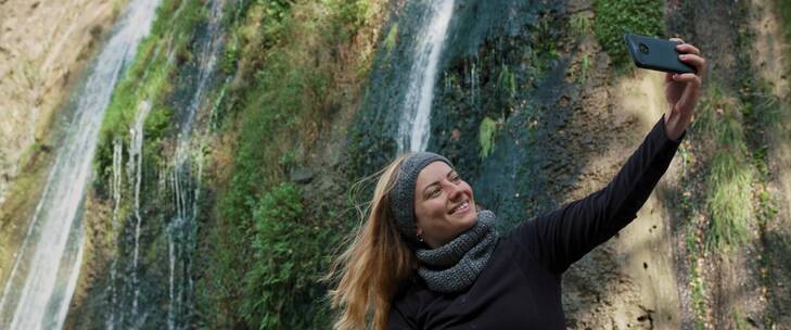 女人开心的用手机与瀑布合照