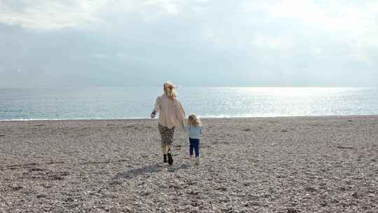 海滩上的秋天母亲和女儿跑向大海或海洋
