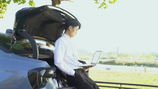 户外靠在汽车后备箱的年轻男性使用电脑视频素材模板下载