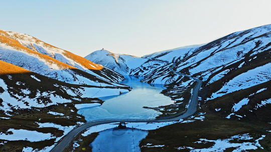 大海草山夕阳下结冰的湖面积雪的草山航拍