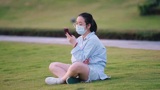 坐草地上玩手机的女子