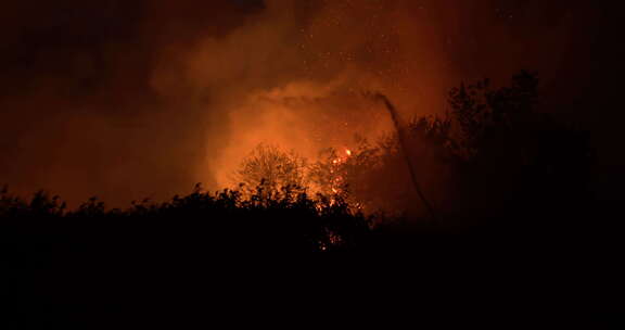 夜间在田野上燃烧草地。消防员在