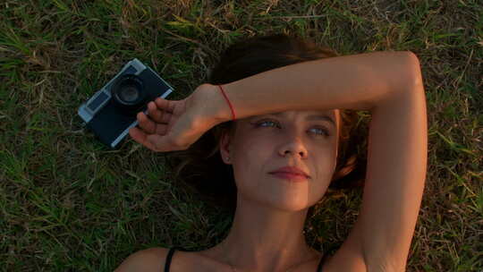 年轻女子躺在草地上用复古相机