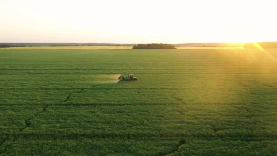 夕阳下田地里拖拉机为粮食作物施肥航拍