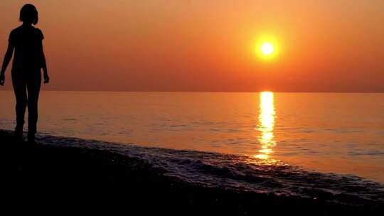 夕阳背景下女孩走过海边的剪影