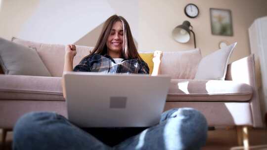 年轻女子坐在地板上的莲花位置，笔记本电脑看着屏幕，钦佩地微笑着