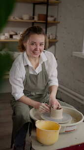 一个穿着粘土围裙的女陶工在陶器上塑造陶罐
