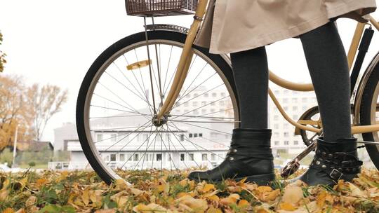 穿着黑靴的女人推着自行车走在秋天的路上视频素材模板下载