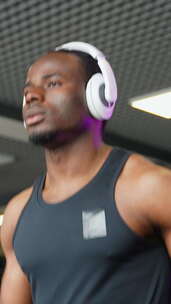 一个戴耳机的男人在跑步机上的现代健身房跑