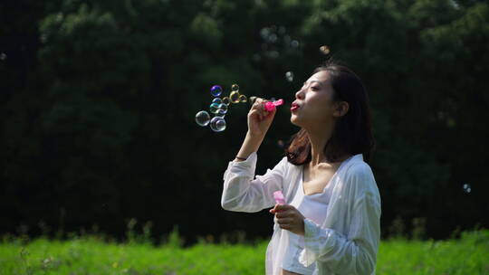 年轻美丽的女孩在草地上玩吹泡泡