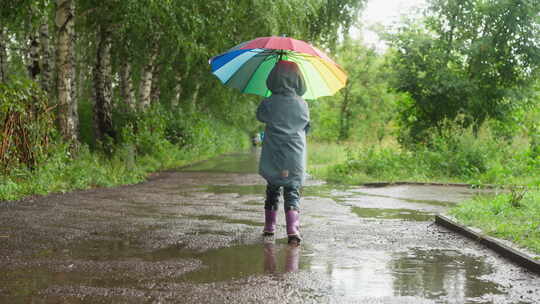 孩子带着雨伞漫步在公园里