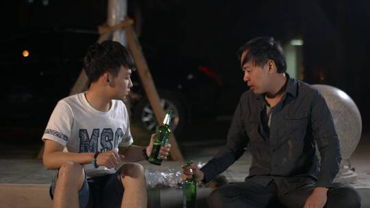 两男子坐在路边喝啤酒