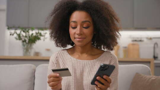 快乐微笑的非裔美国女性手持手机和信用卡购