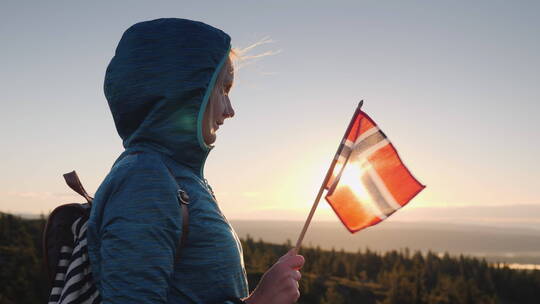 手里拿着挪威国旗的女孩在山顶遇见日出