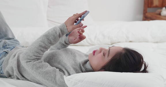 年轻女孩躺在床上玩手机刷视频