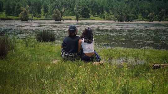 情侣坐在草地小河边背影