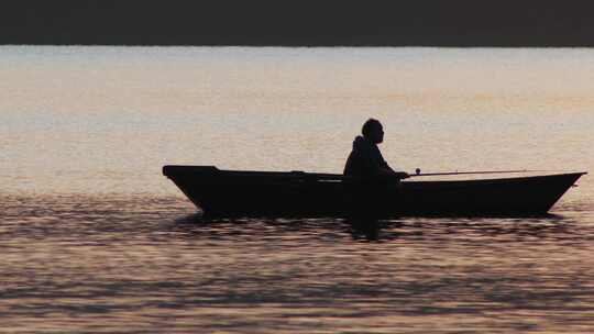 日落时坐在船上钓鱼的人