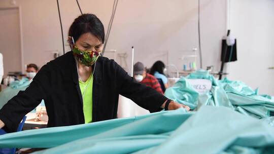 工人带着口罩在小工厂生产防护服和口罩