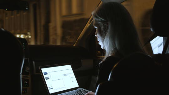 女商人晚上在车里使用笔记本电脑的背面视图