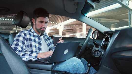 年轻人用笔记本电脑工作，在车里拿着咖啡慢