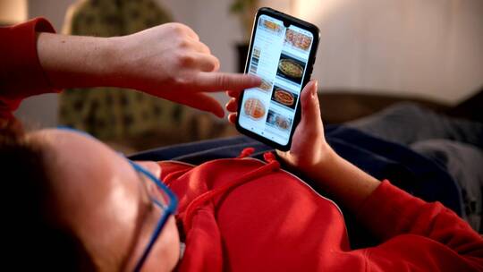 躺在床上的一名男子在手机上滚动食物图片