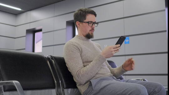 男人坐在公共椅子上玩手机视频素材模板下载
