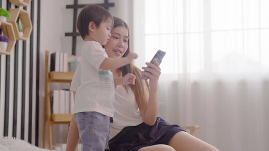 亚洲母亲在床上和孩子一起享受乐趣使用手机