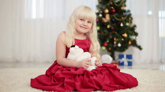 抱泰迪熊的女孩坐在圣诞树旁