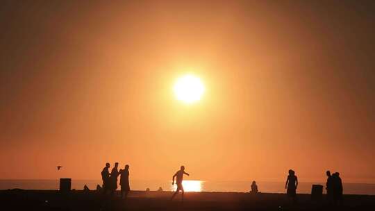 日落时分，圣莫尼卡海滩上，十几岁的男孩在踢美式足球。