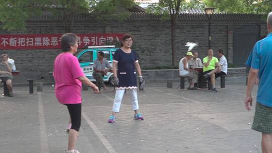 慢动作广场老人健身踢剪子年轻人打羽毛球视频素材模板下载
