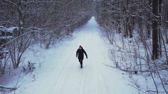 冬季森林中戴着圣诞老人帽子行走的人鸟瞰雪