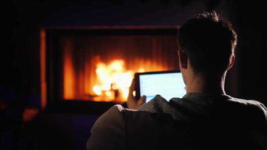 夜晚男人坐在壁炉前玩平板电脑