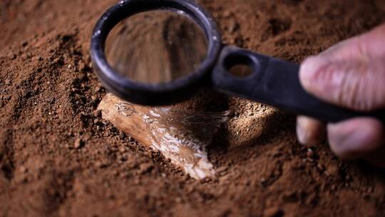 考古人员野外用放大镜观察研究埋在沙土文物