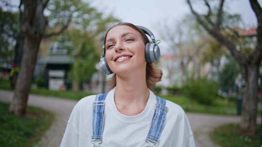 漫步的女人在绿色公园用无线耳机听音乐特写