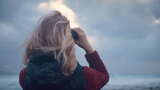 暴风雨天气中，女人站在海边，用双筒望远镜高清在线视频素材下载