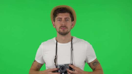 度假戴帽子的游客肖像在复古相机上拍照。绿屏