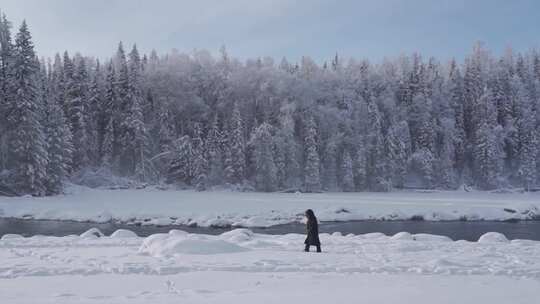 女人走在大雪覆盖的新疆喀纳斯河边