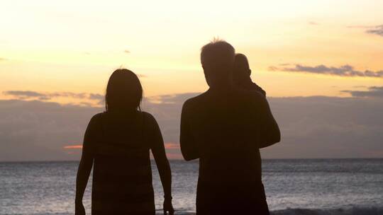 日落时分沿着海滩散步的家庭剪影