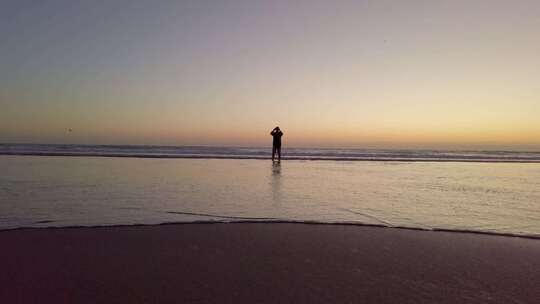 日落时一个男人沿着海洋散步的剪影