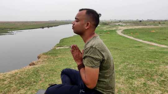 一个亚洲男孩坐在莲花位置祈祷和冥想的侧视图。面对河边