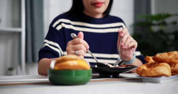 年轻的亚洲女人在家里的餐桌上享受美食。