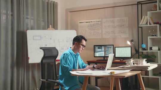 亚洲男工程师在笔记本电脑上打字，走出办公室前看着蓝图