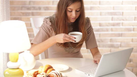 迷人的女孩坐在咖啡馆里玩电脑喝咖啡