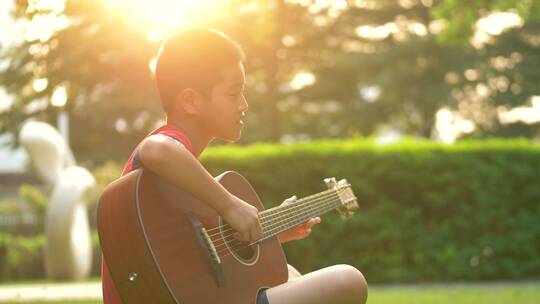 傍晚时分坐在小区草地上弹琴的小男孩侧脸