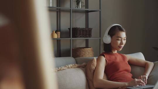 坐在沙发上戴耳机玩笔记本电脑的女人