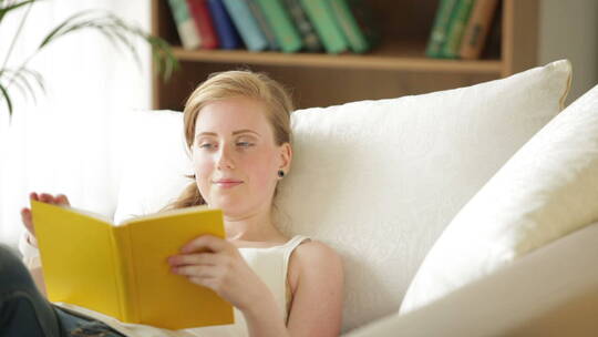 美丽的金发女孩放松的躺在沙发上看书