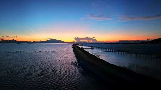 航拍夕阳下汽车开灯行驶在有晚霞的海边