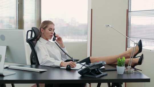 女经理坐在办公室的工作场所，腿放在桌子上打电话