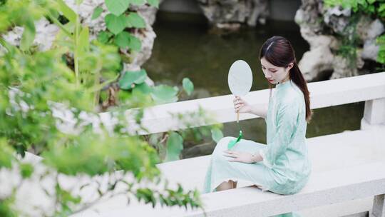 身穿汉服年轻女子摇着扇在景观池边休息纳凉视频素材模板下载